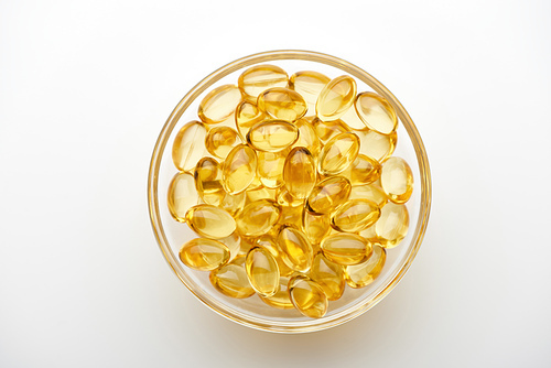 top view of golden fish oil capsules in glass bowl on white background