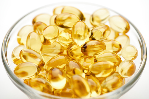 close up view of golden fish oil capsules in glass bowl on white background