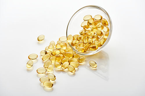 golden fish oil capsules in glass bowl on white background
