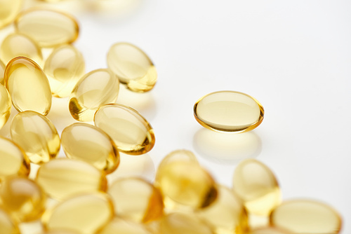 close up view of golden fish oil capsules scattered on white background
