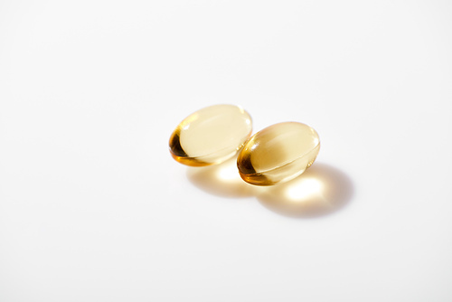 two golden fish oil capsules on white background
