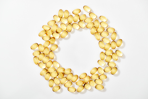 top view of golden fish oil capsules arranged in round frame on white background