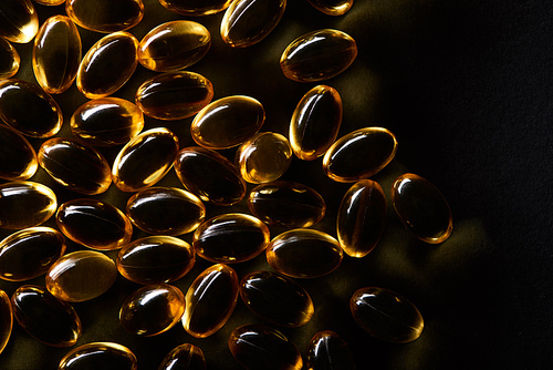 top view of golden fish oil capsules on black background in dark
