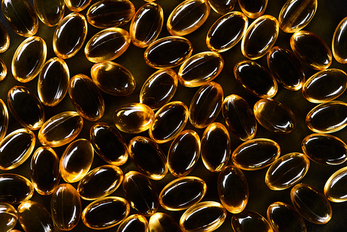top view of golden fish oil capsules on black background in dark