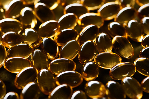 close up view of shiny golden fish oil capsules on black background in dark