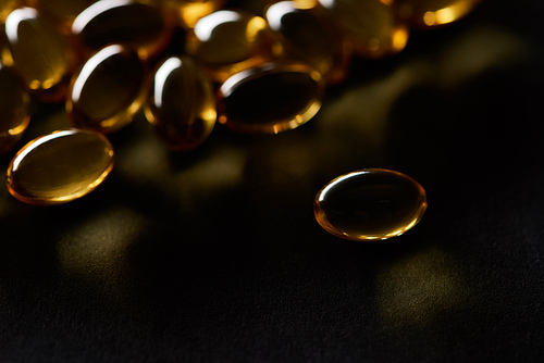 close up view of golden fish oil capsules on black background in dark