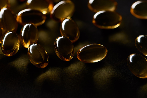 close up view of golden fish oil capsules on black background in dark