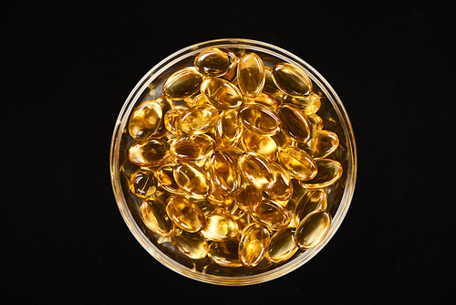 top view of golden fish oil capsules in glass bowl isolated on black