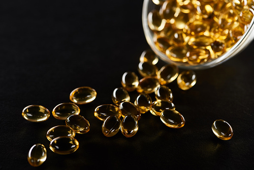 selective focus of golden fish oil capsules in glass bowl isolated on black