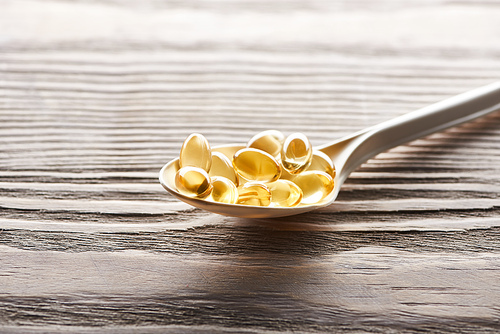 golden fish oil capsules in spoon on wooden table