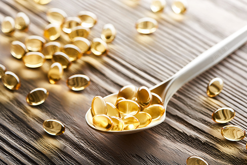 golden fish oil capsules in spoon and on wooden table
