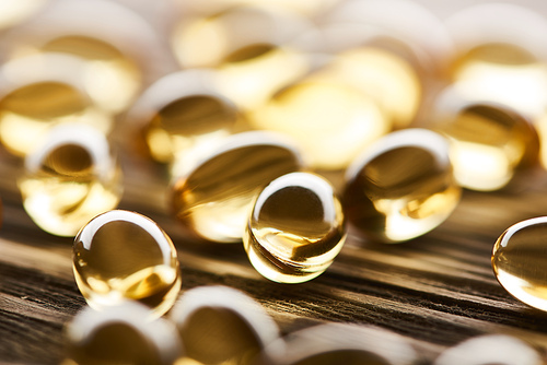 close up view of golden fish oil capsules scattered on wooden table