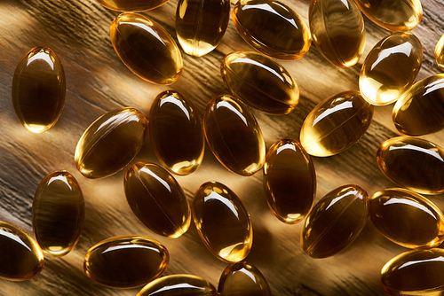 shiny golden fish oil capsules scattered on wooden table in dark