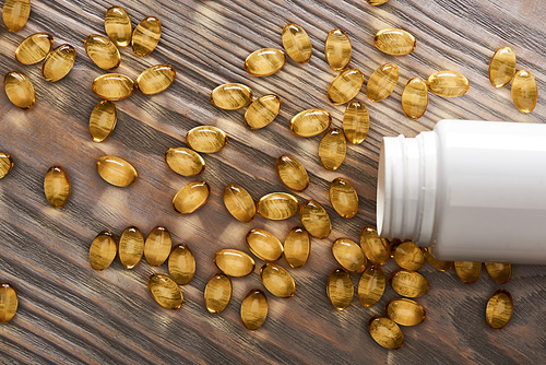 golden fish oil capsules scattered from plastic container on wooden table