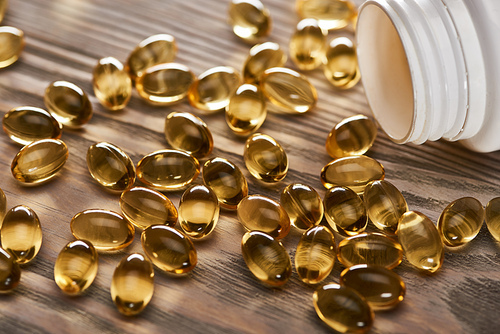 golden fish oil capsules scattered from plastic container on wooden table
