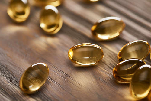 close up view of shiny golden fish oil capsules scattered on wooden table