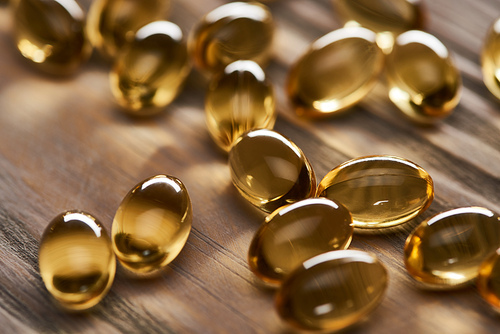 close up view of shiny golden fish oil capsules scattered on wooden table