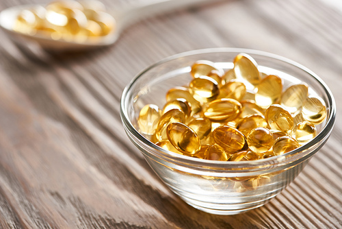 selective focus of golden fish oil capsules in glass bowl and spoon on wooden table