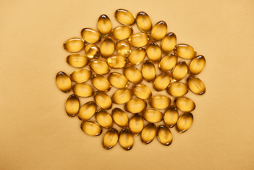 top view of golden shiny fish oil capsules on yellow background