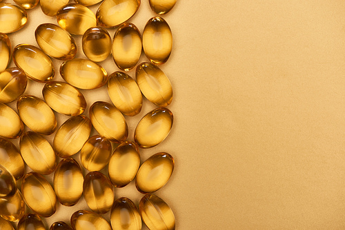 top view of golden shiny fish oil capsules on yellow background with copy space