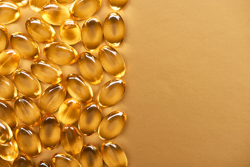 top view of golden shiny fish oil capsules on yellow background with copy space