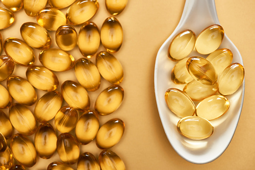 top view of golden shiny fish oil capsules in spoon on yellow background