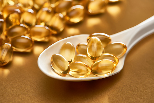 close up view of shiny fish oil capsules in spoon on golden background