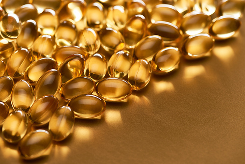 close up view of shiny fish oil capsules on golden background with copy space