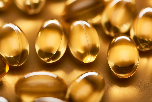 close up view of shiny fish oil capsules on golden background