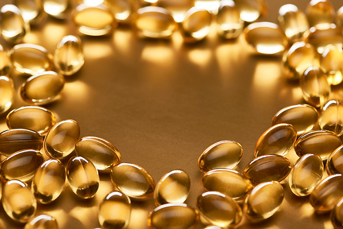 close up view of shiny fish oil capsules on golden background with copy space
