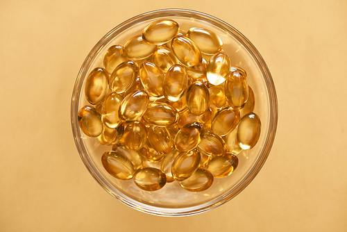 top view of shiny golden fish oil capsules in glass bowl on yellow background