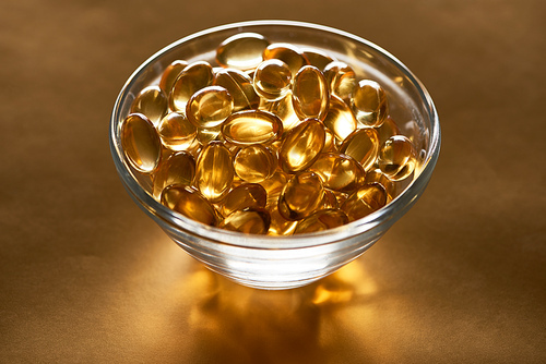 shiny fish oil capsules in glass bowl on golden background