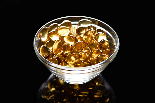 golden shiny fish oil capsules in glass bowl on black background