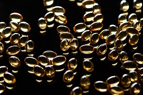 shiny golden fish oil capsules scattered on black background