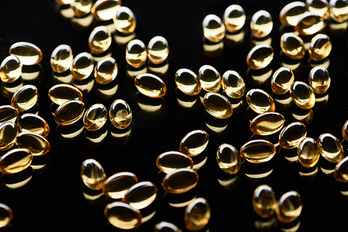 shiny golden fish oil capsules scattered on black background