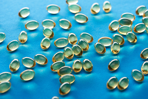 golden fish oil capsules scattered on blue background