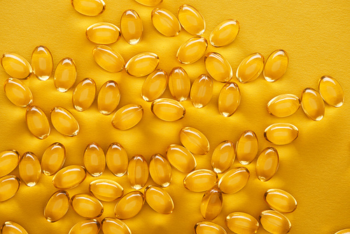 top view of golden shiny fish oil capsules scattered on yellow bright background
