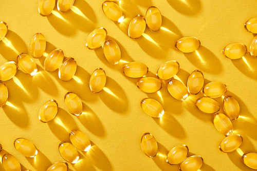 top view of golden shiny fish oil capsules scattered on yellow bright background