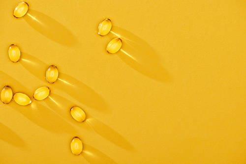 top view of golden shiny fish oil capsules scattered on yellow bright background with copy space