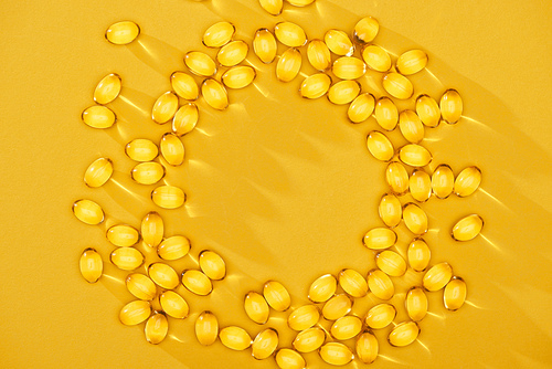 top view of golden shiny fish oil capsules arranged in circle on yellow bright background with copy space