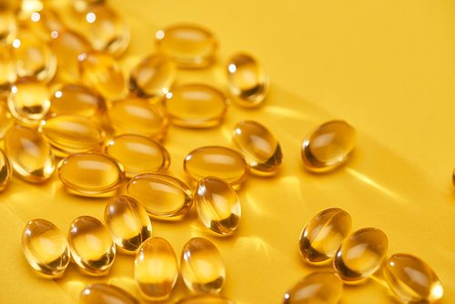 close up view of golden shiny fish oil capsules scattered on yellow bright background