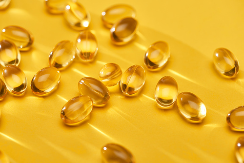close up view of golden shiny fish oil capsules scattered on yellow bright background