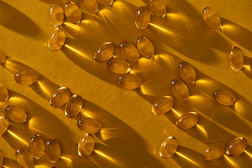 golden shiny fish oil capsules scattered on yellow background in dark
