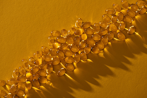 top view of golden shiny fish oil capsules on yellow background in dark