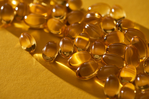 close up view of golden shiny fish oil capsules scattered on yellow background in dark