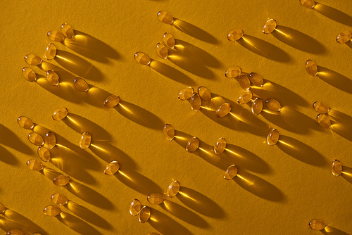 top view of golden shiny fish oil capsules scattered on yellow background in dark