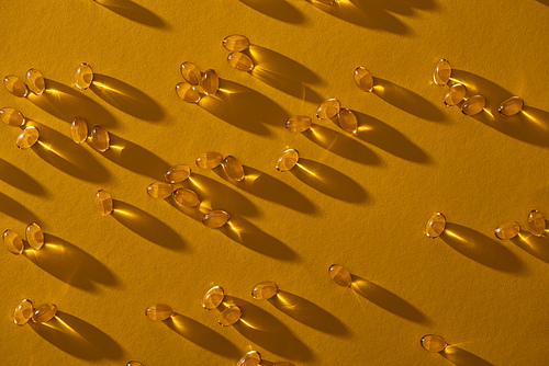 top view of golden shiny fish oil capsules scattered on yellow background in dark