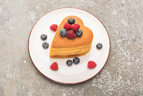 heart shaped pancakes with berries on plate on grey concrete surface
