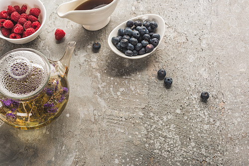 top view of berries, herbal tea and maple syrup on grey concrete surface