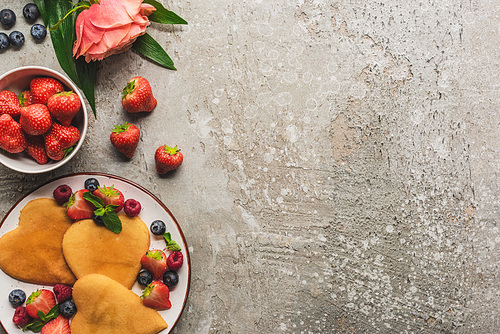 top view of heart shaped pancakes with berries on grey concrete surface with blooming rose